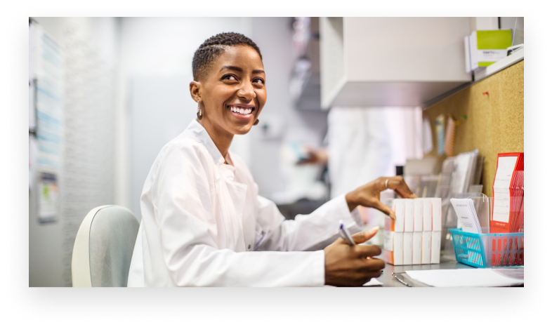 Female chemist sitting at her desk and looking away smiling. African woman pharmacist working at her desk.
