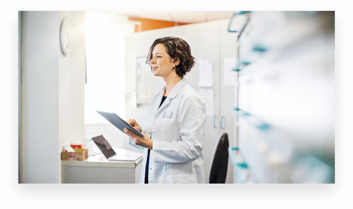 A serious female doctor sits at a conference table during a staff meeting. She gestures as she speaks with an unrecognizable coworker. The coworker also gestures.